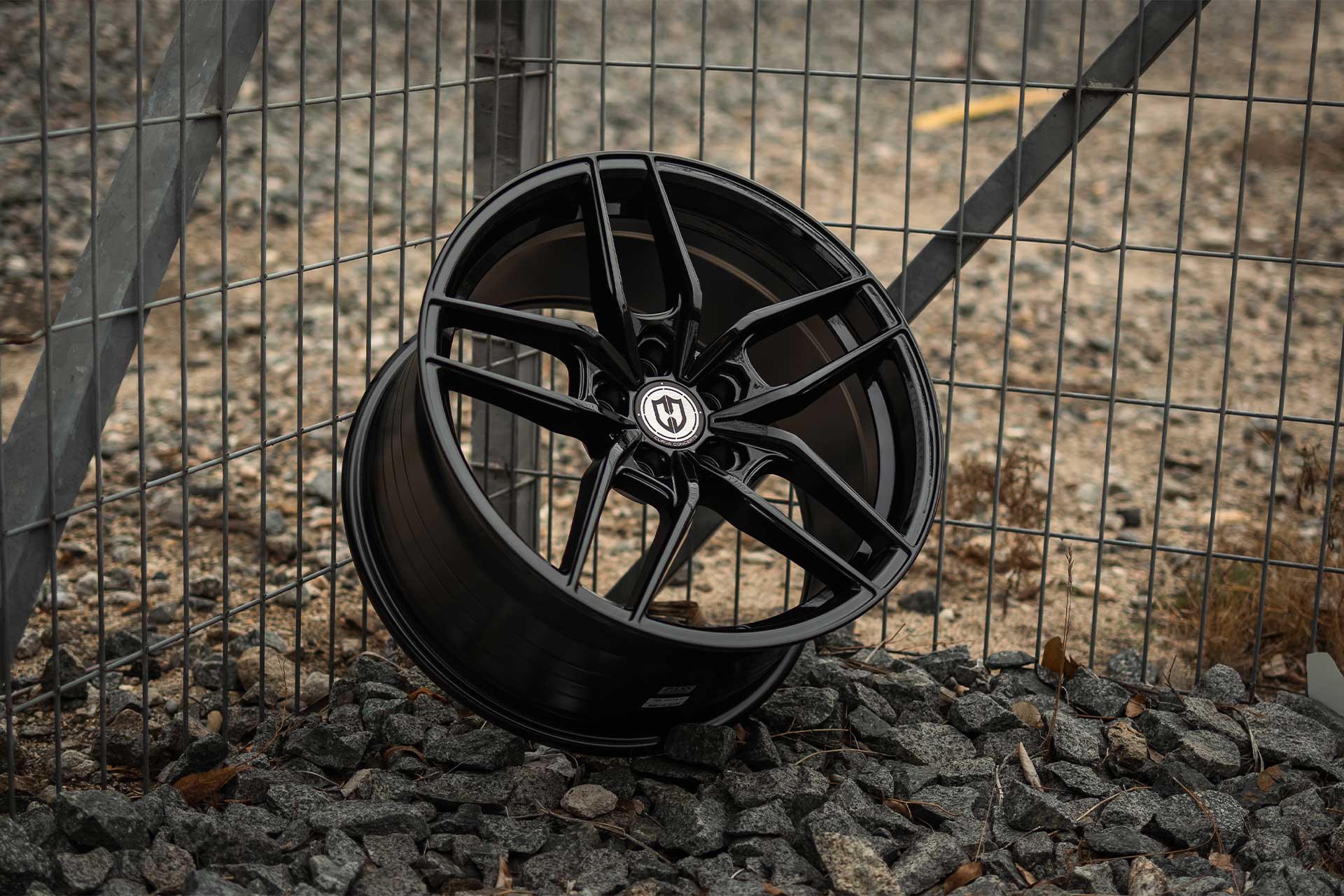 gloss black curva concepts cff25 wheel on gray rocks against a metal fence