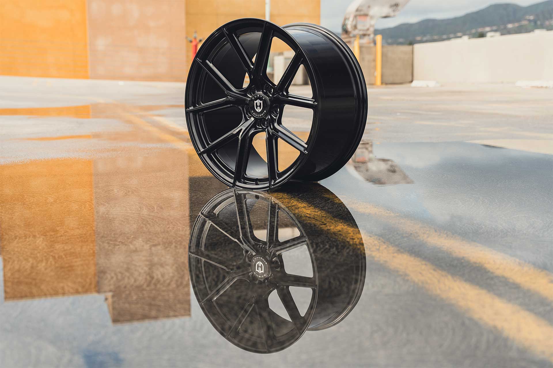 shot of a gloss black curva concepts cff70 wheel in a puddle of water with its reflection in the puddle