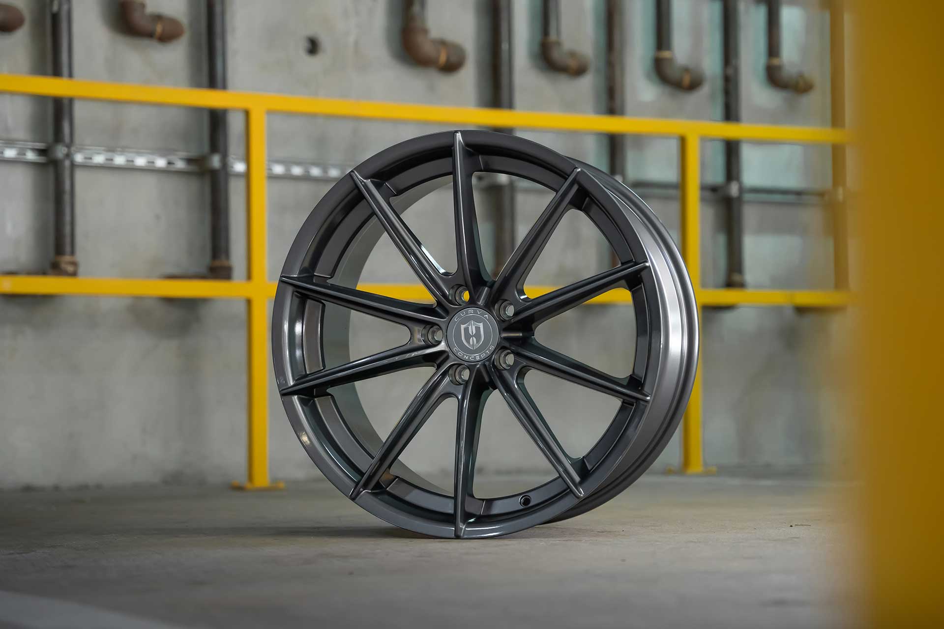 close up shot of a gunmetal curva concepts cff46 wheel in a concrete garage with yellow railings in the background